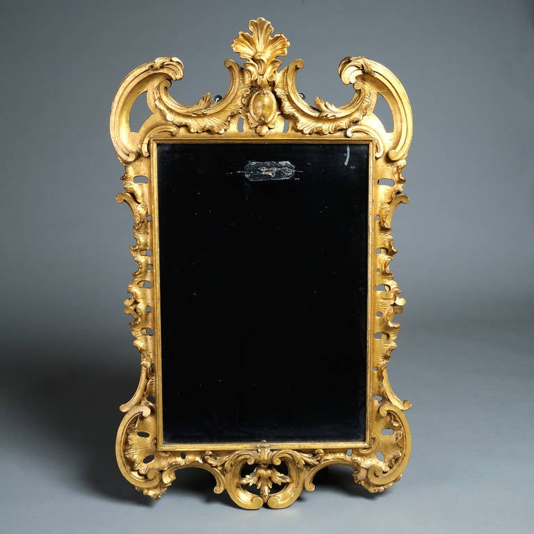 A George II giltwood mirror with original bevelled plate in a pierced rocaille and scroll-carved frame, circa 1760, re-gilt in the 19th century.