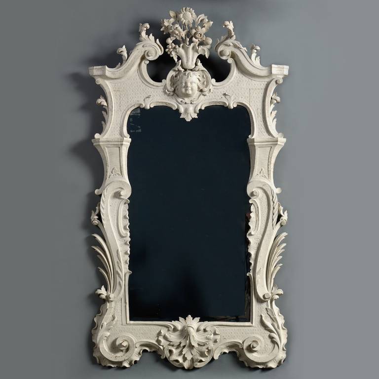 A MAGNIFICENT GEORGE II WHITE-PAINTED MIRROR, CIRCA 1740.
With fine original bevelled rectangular plate, the frame carved with scrolls and foliage and decorated with an incised hatched pattern, the pediment cresting with the mask of a putto