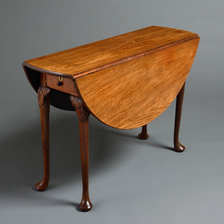 A Chinese export Huang Huali drop-leaf gateleg table, circa 1740. 
With circular drop-leaf top, the frieze with a drawer to either end on cabriole legs carved with shells and foliage and terminating in pad feet.