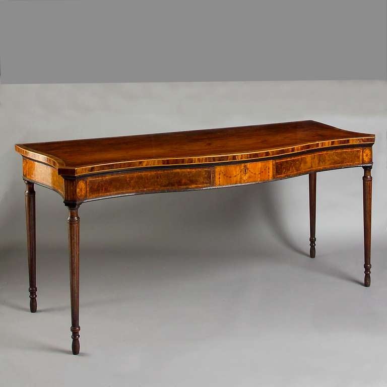 a fine George III mahogany and marquetry serpentine side table, circa 1780.
With crossbanded figured top, the frieze with a satinwood drawer inlaid with husk swags flanked by panels of ‘quilted’ mahogany, the angles inlaid with flutes flanked by