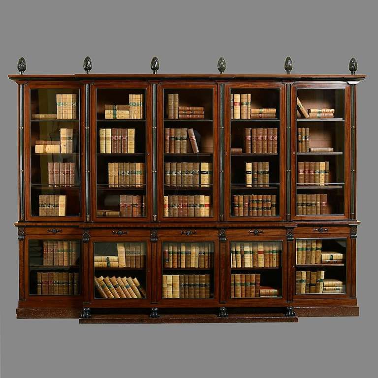 AN EXCEPTIONAL REGENCY BRONZE-MOUNTED AND EBONISED FIGURED MAHOGANY BREAKFRONT BOOKCASE ATTRIBUTED TO ROBERT HERRING, CIRCA 1810.
The stepped cornice with laurel leaf finials above five doors with bronze astragals, divided by bronzed cluster