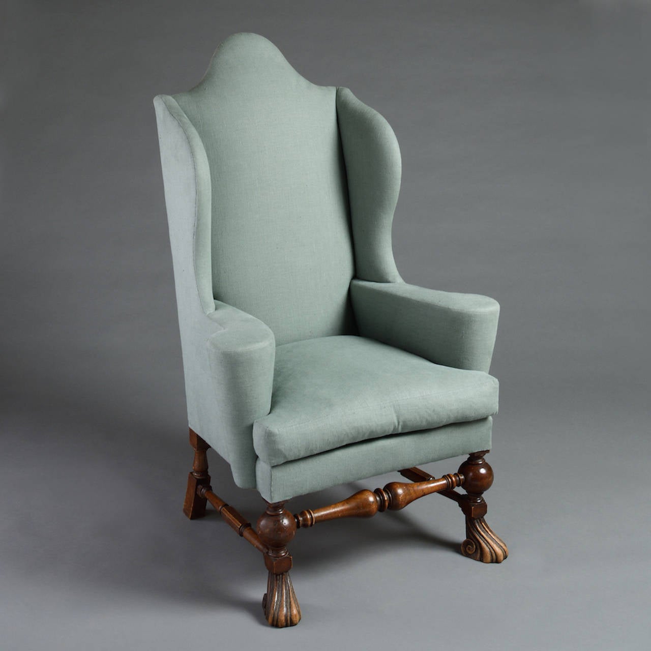 A QUEEN ANNE STYLE WALNUT WING ARMCHAIR WITH ELABORATELY SCROLLED FEET, circa 1910.