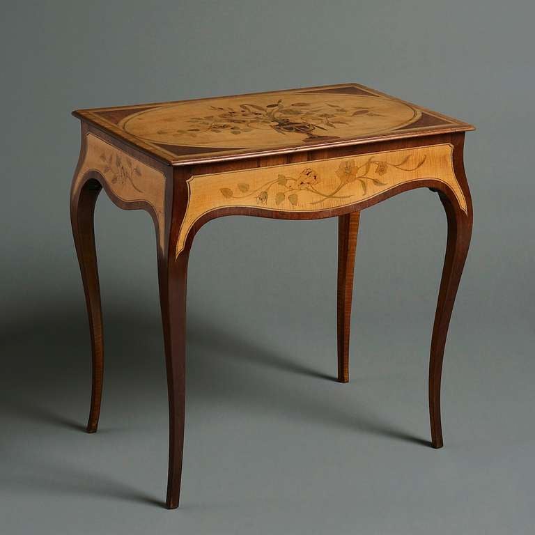 A George III harewood and marquetry lady’s writing table in the manner of John Cobb, circa 1770.
The rectangular top with an oval panel inlaid with a flower-filled urn, the serpentine frieze inlaid with flowers on three sides and fitted with an end