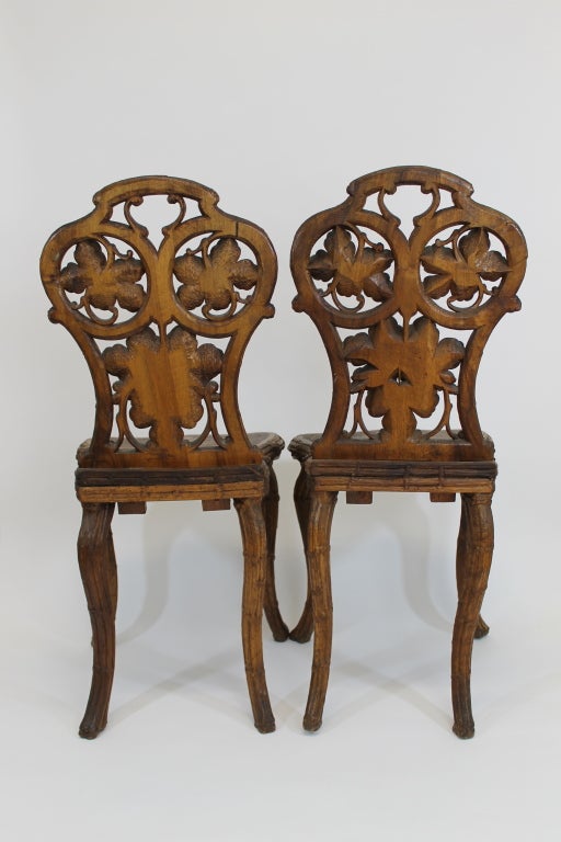 Pair of chestnut wood chairs with grape vine leaf details carved in the tradition of coo coo clocks.