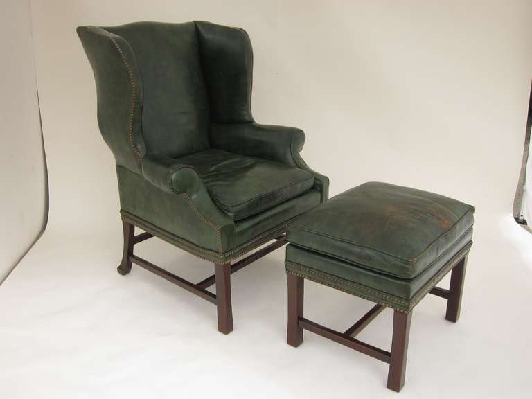 Large English dark green leather wingback armchair and ottoman with brass tacks and nice leather patina.