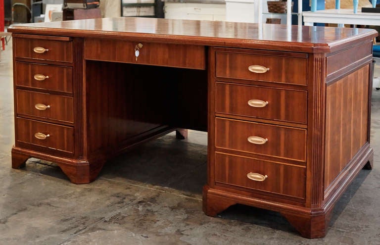 This antique executive desk, composed of solid walnut and rosewood, features  beautiful deco accents, original brass hardware, and pull-out writing trays. With its carved molding trims and inlaid wood table-top, this piece is a gem.  

Restored