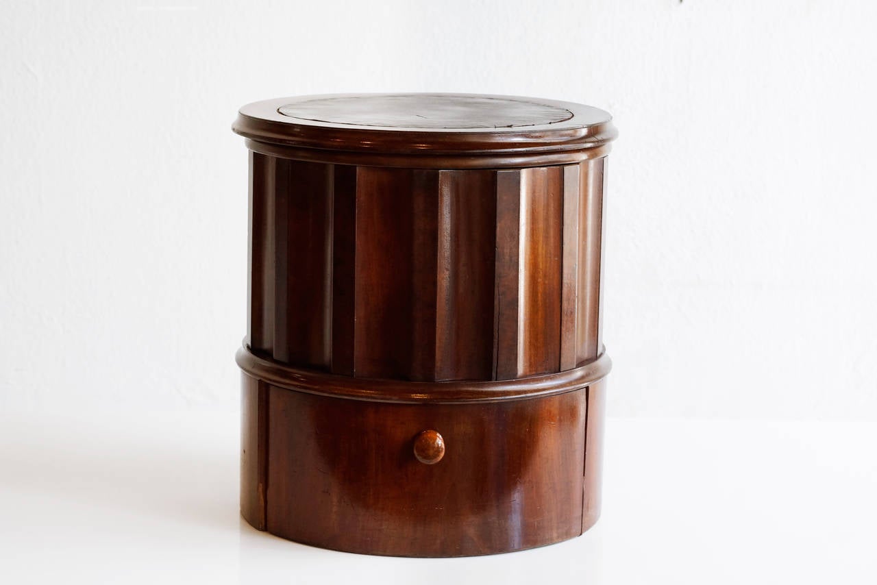 Antique mahogany wood chamber pot or low commode in neoclassical style, c. 19th century.  Cylindrical unit features fluted columnar design with circular hinged lid. Leather inlay on lid and step. Slide out footrest with wooden knob pull.