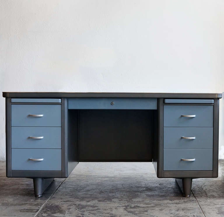 This classic 1950's Steelcase tanker desk features a double pedestal base with adjustable pontoon legs. Newly refinished black linoleum desk-top and two-tone smokey-blue drawers in a natural steel frame. 

Also features: four utility drawers, one