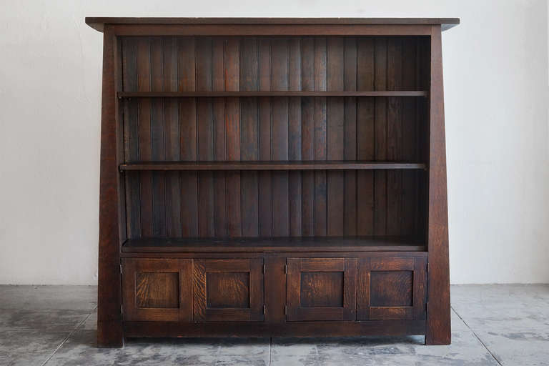 This early 1900's California Craftsman bookcase is composed of solid tiger oak. Unique tapered shape with chamfered slat back. Features two double door cabinets. Impressive in size, this bookcase makes a statement. In the style of Gustav Stickley or