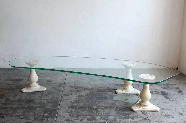 Classicism meets Mid-Century Modern in this elegant and highly unique 1950s coffee table. Large, thick-cut, kidney-shaped glass sits atop three classical wood columns. Stunning from every angle, this piece is a show stopper. Designed by the