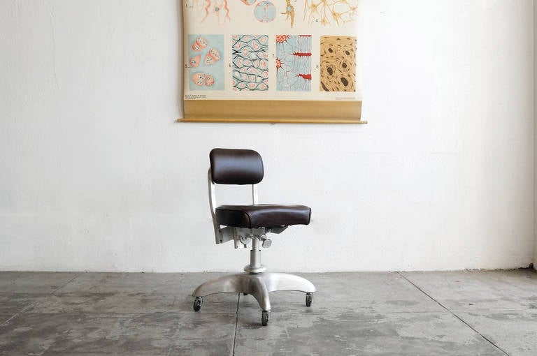 This classic stenographer's task chair features a refinished aluminum frame and reupholstering in brown leather. Swivels, adjusts and rolls on casters. Seat height ranges from 18