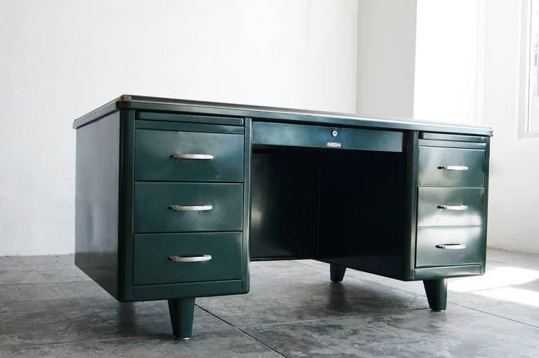 Stunning tanker desk with unique deco accents including a waterfall top and streamline brushed steel handles. Newly refinished in a deep forest green with black linoleum table top

Other features include double pedestal configuration with four