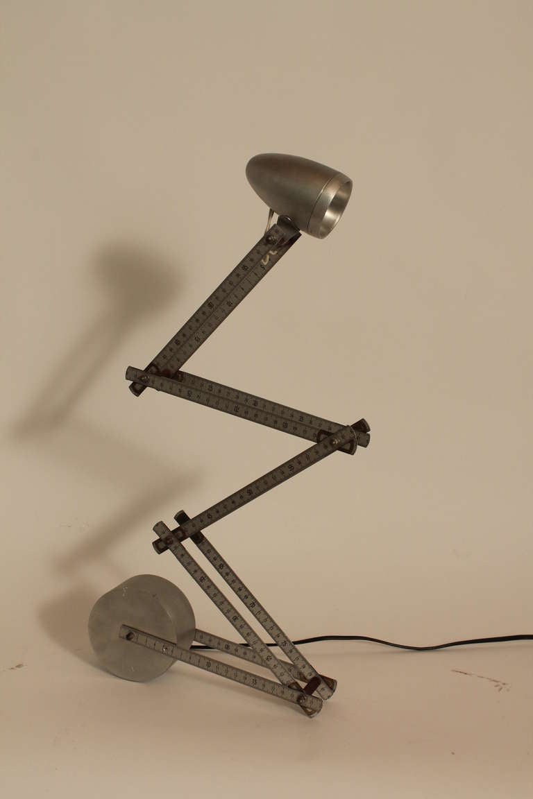 Ingenious table lamp constructed of 2 french metal folding rulers.
The base is an aluminum wheel that is signed AHA.
Height adjusts from 9 inches to 34 inches , depending upon your preference. The head is also adjustable.
There is an in line