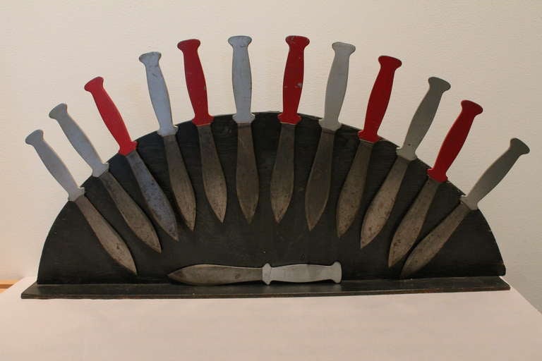 A graphic collection of 13 Circus throwing knives mounted onto a primitive demilune stand. They are very simply wired into the existing array , with one loose and not mounted on the stand.