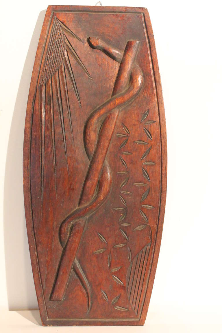 Great folk art plaque carving of a snake entwined rod facing the sun.
The Rod of Asclepius is a serpent-entwined rod wielded by the Greek god Asclepius, a deity associated with healing and medicine. The symbol has continued to be used in modern