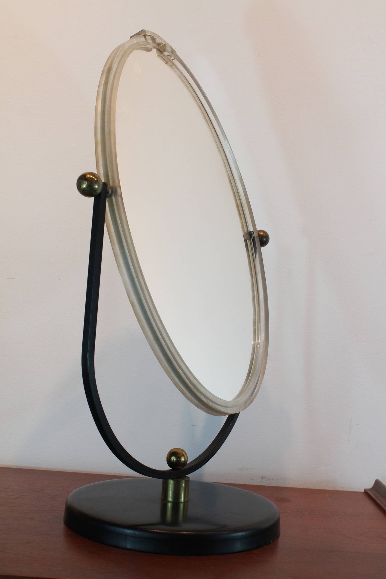 Large scale sculptural Mid-Century Modern lucite framed vanity mirror with ebonized metal base and arms with brass column and ball hinges.
Double sided mirror that can swivel and be tightened in any position.