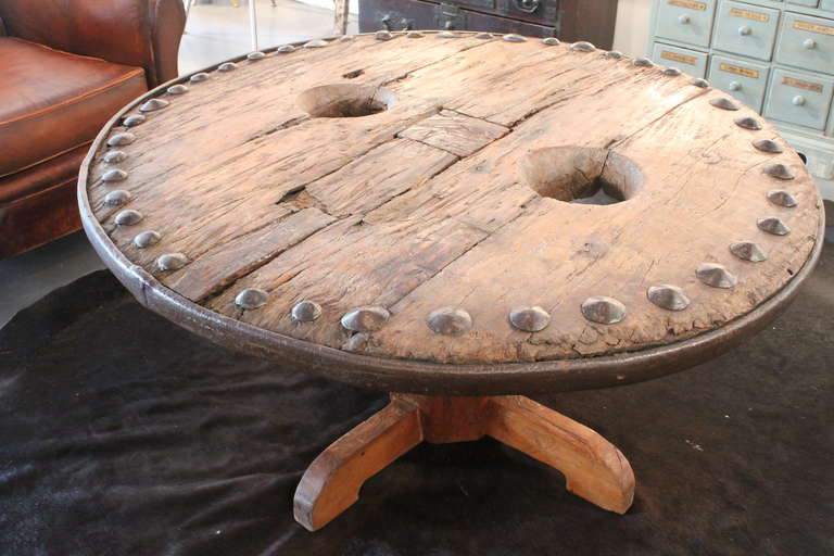 Exceptional wear and form on this ancient iron rimmed wagon wheel converted into a cocktail table. 
The perimeter is surrounded with hand forged iron buttons.