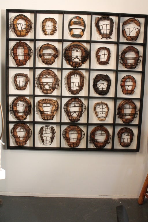 This display is a collection of 25 mounted catcher's masks onto a framed grid work.
The catcher's masks are mostly early to mid 20th century and are individually mounted onto the backing board and surrounded with the frame , so it is a single unit