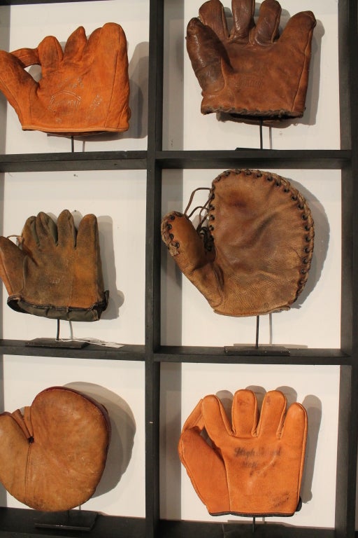 This display is a collection of 9 baseball gloves , each with its own individual stand, set in a framed grid display.
The baseball mitts are mostly early to mid 20th century and can be interchanged in the individual cubbies.