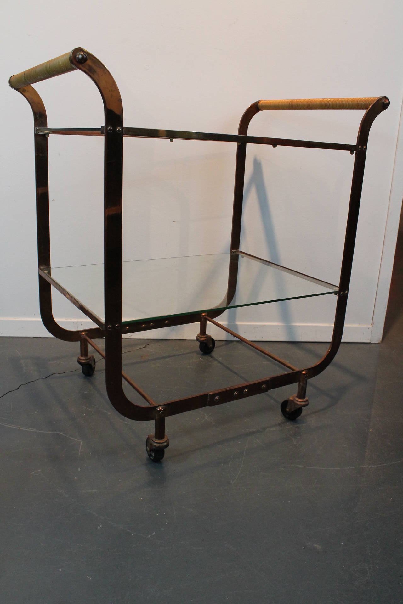 Amazing Art Deco bar cart in copper with rattan wrapped handles.
2 tiered glass shelves with brass casters.