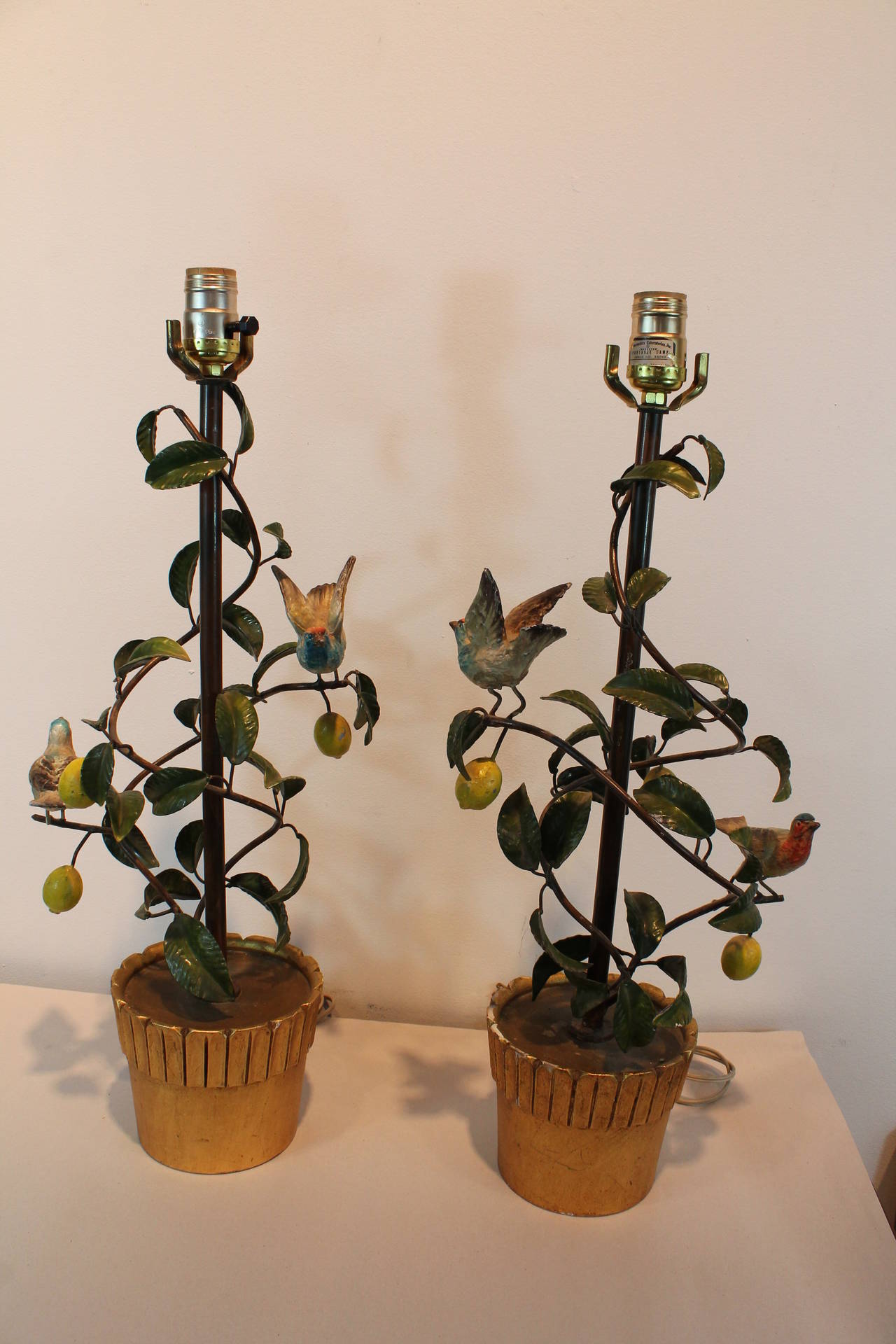 Great pair of whimsical tole lamps.
In each lamp there are birds perched in a lemon tree with the base of the lamp being a gilt and gessoed ceramic planter.
Great color and strong sculptural form of the tree wrapping around the center post.