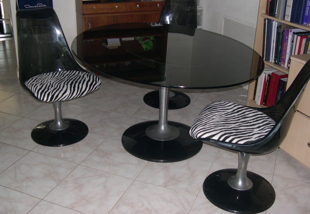  A dining set of a tulip shape table with an oval shape dark glass top in the style of Saarinen and two swivel lucite chairs.