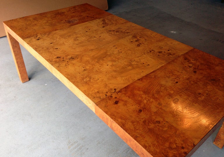 A dining table with two central extension leaves designed by Milo Baughman. Veneered in book-matching olive burl wood. Simple Parson style. With matching credenza and chairs.