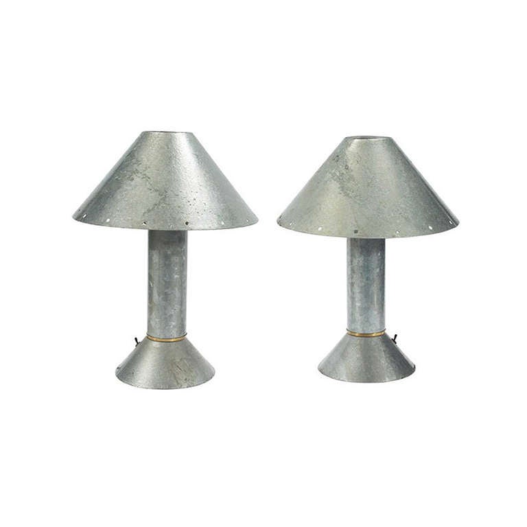 A pair of rare table lamps designed by Ron Rezek, a famed industrial designer, circa 1980s. They are constructed with patinated Zinc and brass accent, reminiscent of the zinc tables designed by John Dickinson. The shade is adorned with cutout to