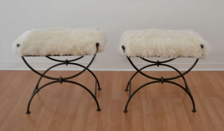 Stunning pair of custom-made Hollywood Regency style wrought iron benches, circa 1950s-1960s. These highly decorative stools are exquisitely designed with woven hand-wrought mesh seats and accented with Mongolian lamb cushions.