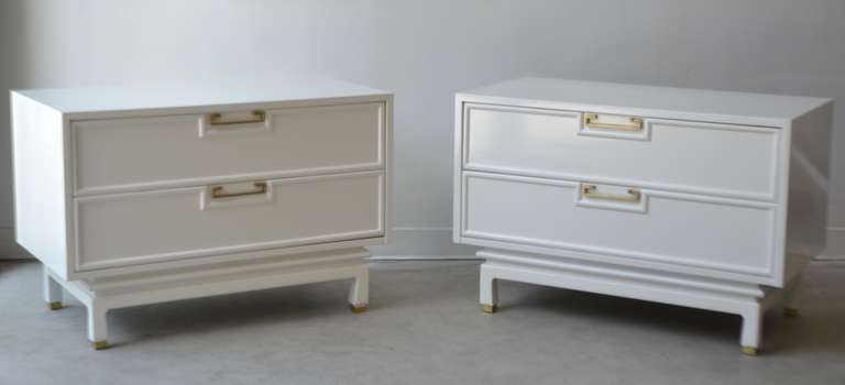 Stunning pair of Hollywood Regency style white lacquered side tables with brass hardware by American of Martinsville, c. 1960s. These incredible Mid Century Modern Asian inspired night stands / bedside tables are designed with two drawers with drop