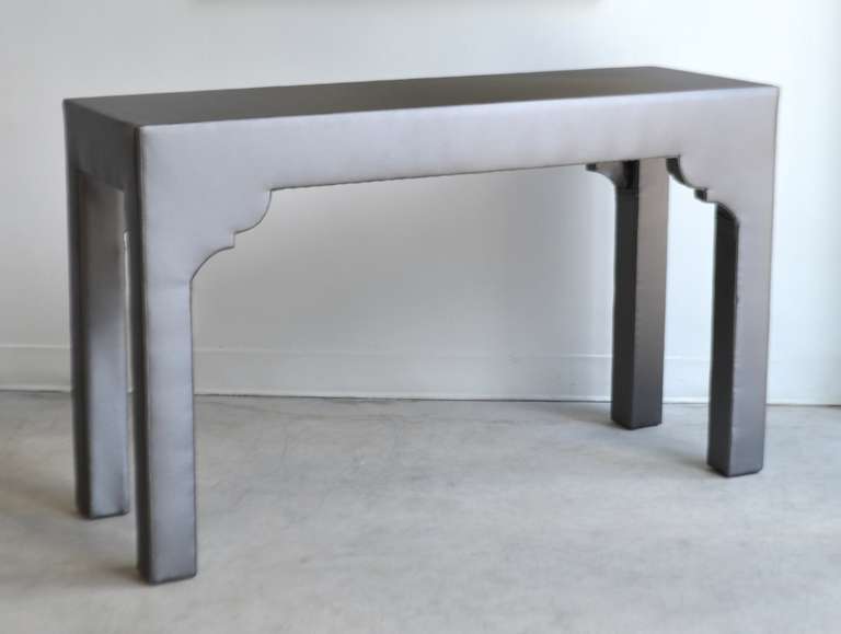 Unique console table upholstered in gray satin eco leather, c. 1960s - 1970s. This striking and dramatic Hollywood Regency style faux leather sofa table is custom designed with decorative modified scalloped detailing.