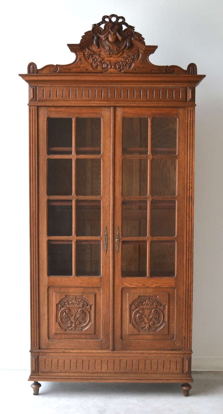 Impressive French carved oak bookcase / display cabinet, c.19th century. This brilliant artisanally carved cabinet with magnificent detail is accented with two glass front doors, brass decorative hardware, four adjustable shelves and has a beautiful