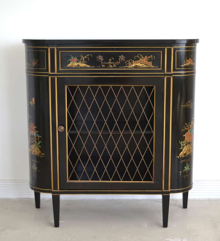 Stunning black lacquered chinoiserie decorated chest with brass mesh door and gilt decorated accents, c. 1940s - 1950s.  This incredible Hollywood Regency style cabinet has one drawer over a decorative brass cross hatch mesh door.
Visit our