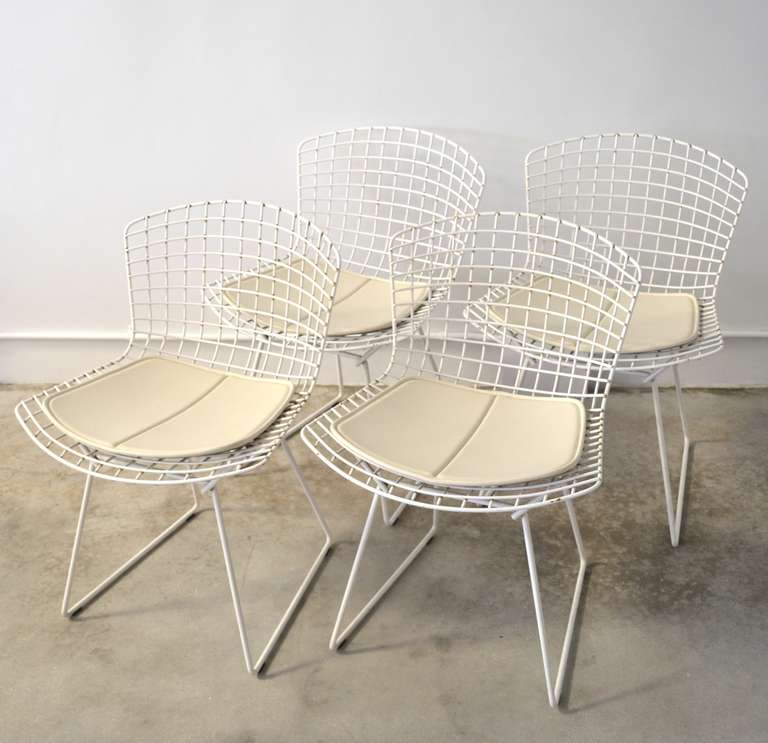 Set of four architectural welded mesh white powder coated dining chairs with white vinyl seat cushions by Harry Bertoia for Knoll, c. 1980s. These sculptural chairs are perfect for indoor or outdoor use.