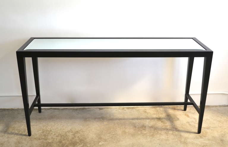 Stunning Hollywood Regency Style black lacquered console table with beveled mirror top in the style of Edward Wormley, c. 1950s - 1960s. This handsome sofa table was designed with tapered legs creating a sleek silhouette.