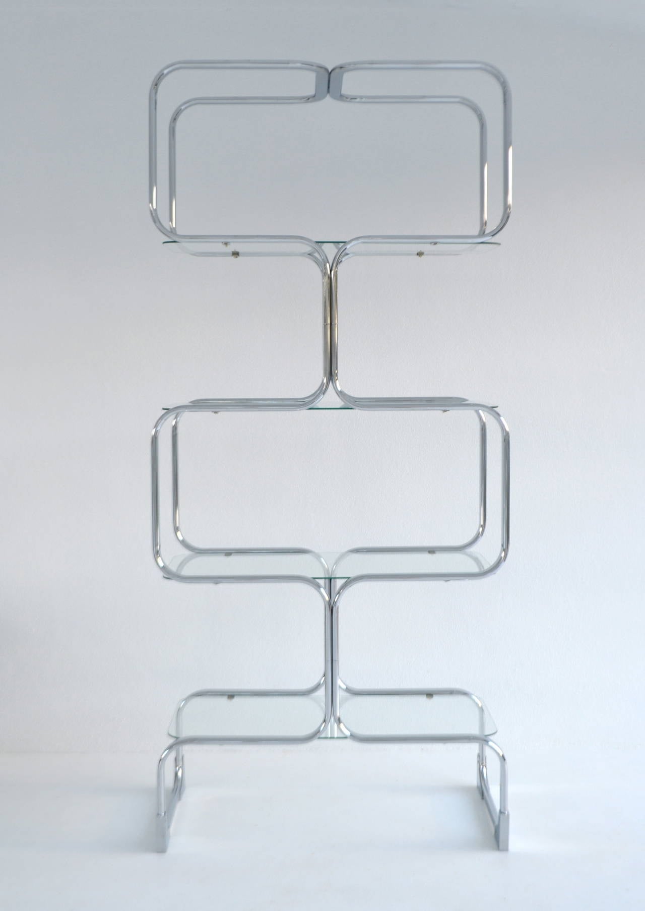 Strikingly graphic chrome etagere by Tricom, Italy, circa 1960s-1970s. This sleek Post-Modern bookshelf is designed and accented with four custom round cornered glass shelves.

Measurements:
Overall: 79