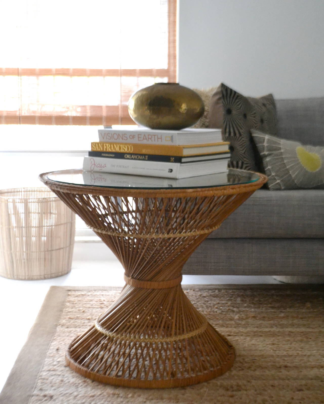 Striking pair of natural woven rattan hour glass side tables, circa 1960s -1970s. These incredible Mid-Century Modern end tables / night stands are designed of intricately webbed rattan and outfitted with round glass tops.