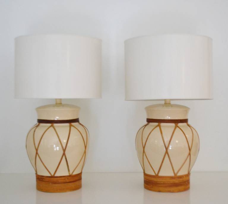 Glamorous pair of butter glazed ceramic jar form table lamps, circa 1960s-1970s. These striking Hollywood Regency style lamps are decorated with bamboo woven accents and wired with brass fittings. Height can be adjusted by adding a smaller or larger