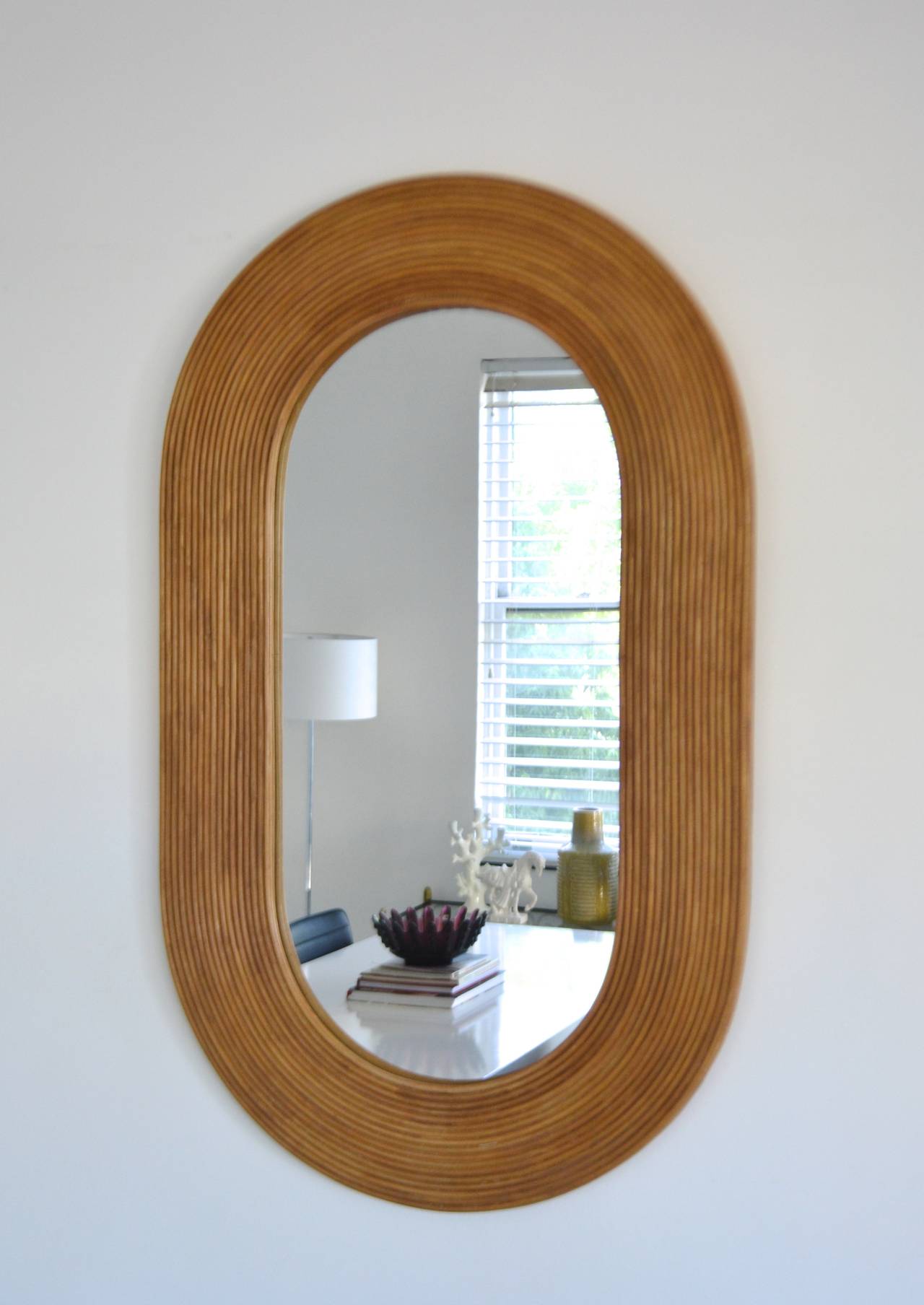 Impressive Mid Century Modern custom oval faux bamboo wall mirror, c. 1970s. This highly decorative carved wooden mirror is designed to capture the glamorous essence of reeded bamboo. 

Measurements: 
Overall: 45