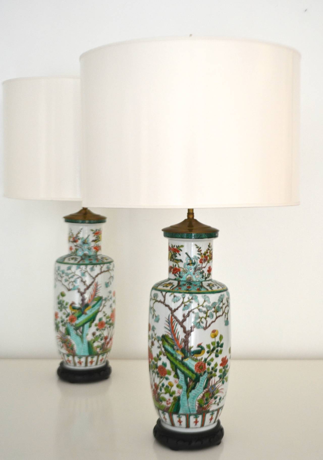 Stunning pair of porcelain Chinoiserie vase form polychrome table lamps, c.1940s - 1950s. These highly decorative Chinese lamps are mounted on carved wooden bases and wired with brass double cluster adjustable fittings.
Shades not