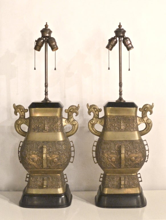 Exceptional patinated bronze urn form Asian-inspired table lamps with custom made ebonized bases and capitals by Marbro, c. 1950s -1960s. These Hollywood Regency style lamps decorated in brass relief are rewired with brass fittings and silk cords.