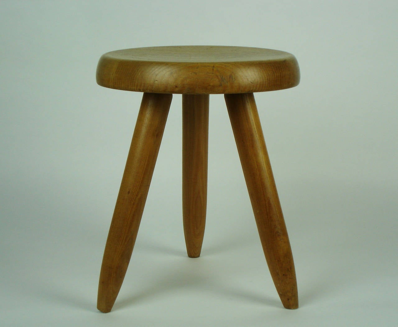 An ash tripod stool designed by Charlotte Perriand.