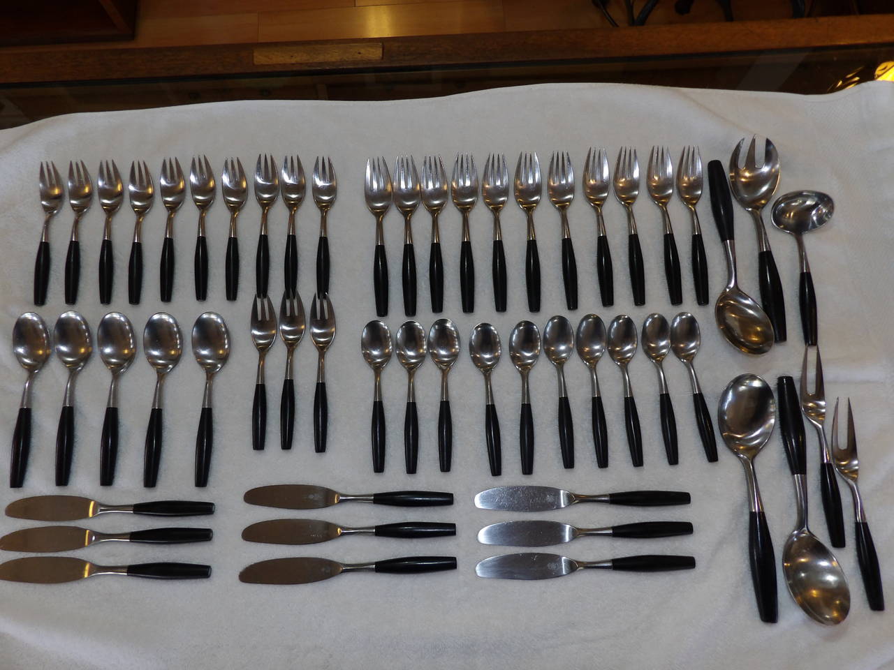 An incomplete service consisting of 55 signed pieces of Danish modern flatware designed by Jens Quistgaard for Dansk, Denmark, circa 1960s. Substantial and graceful stainless steel utensils with ebonized wooden handles. Consisting of seven serving