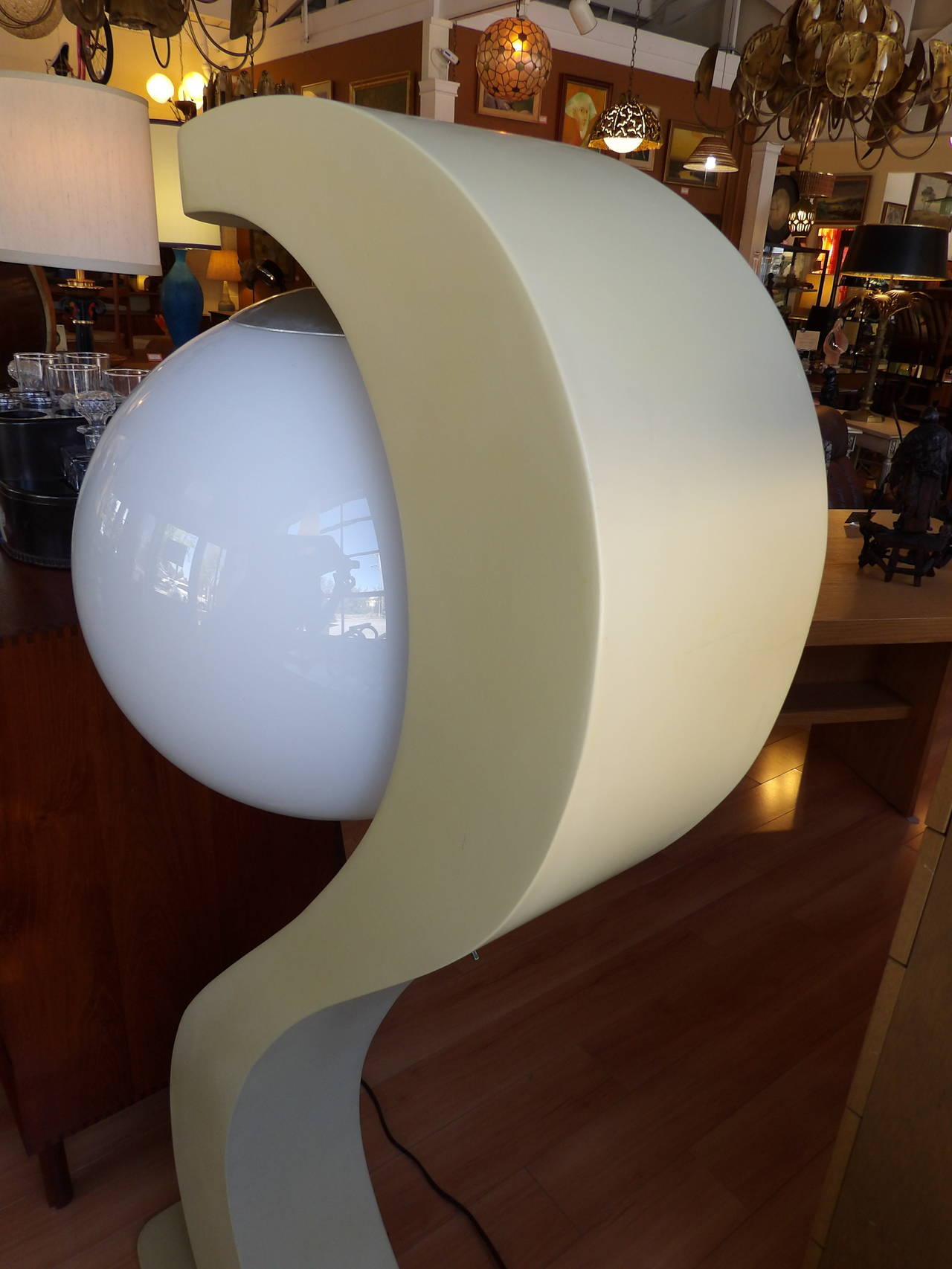 A captivating 1970's mod sculptural floor lamp by Modeline. Hollow painted wood base with a milk glass spherical shade. 
