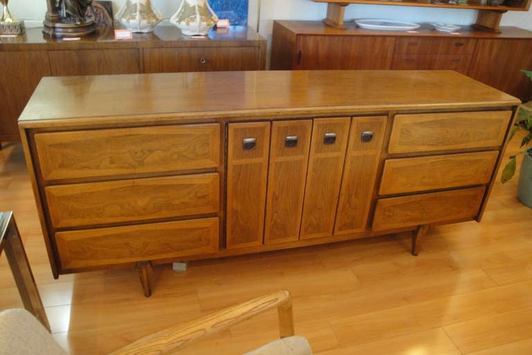 Long, low walnut dresser by American of Martinsville. Center doors open to reveal 3 drawers. Unusual hourglass veneer detail. Could also be used as a credenza.