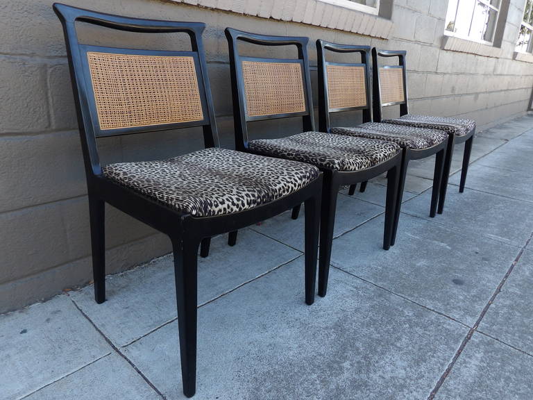 A set of four ebonized dining chairs by John Stuart. Cane back seats with faux leopard skin upholstery.