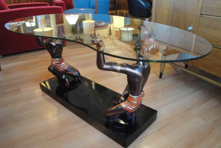 In exceptional original condition is this cast metal Nubian coffee table with an asymmetrical glass top. Two kneeling male figures holding glass top overhead. Made by The California Lamp & Shade Company.