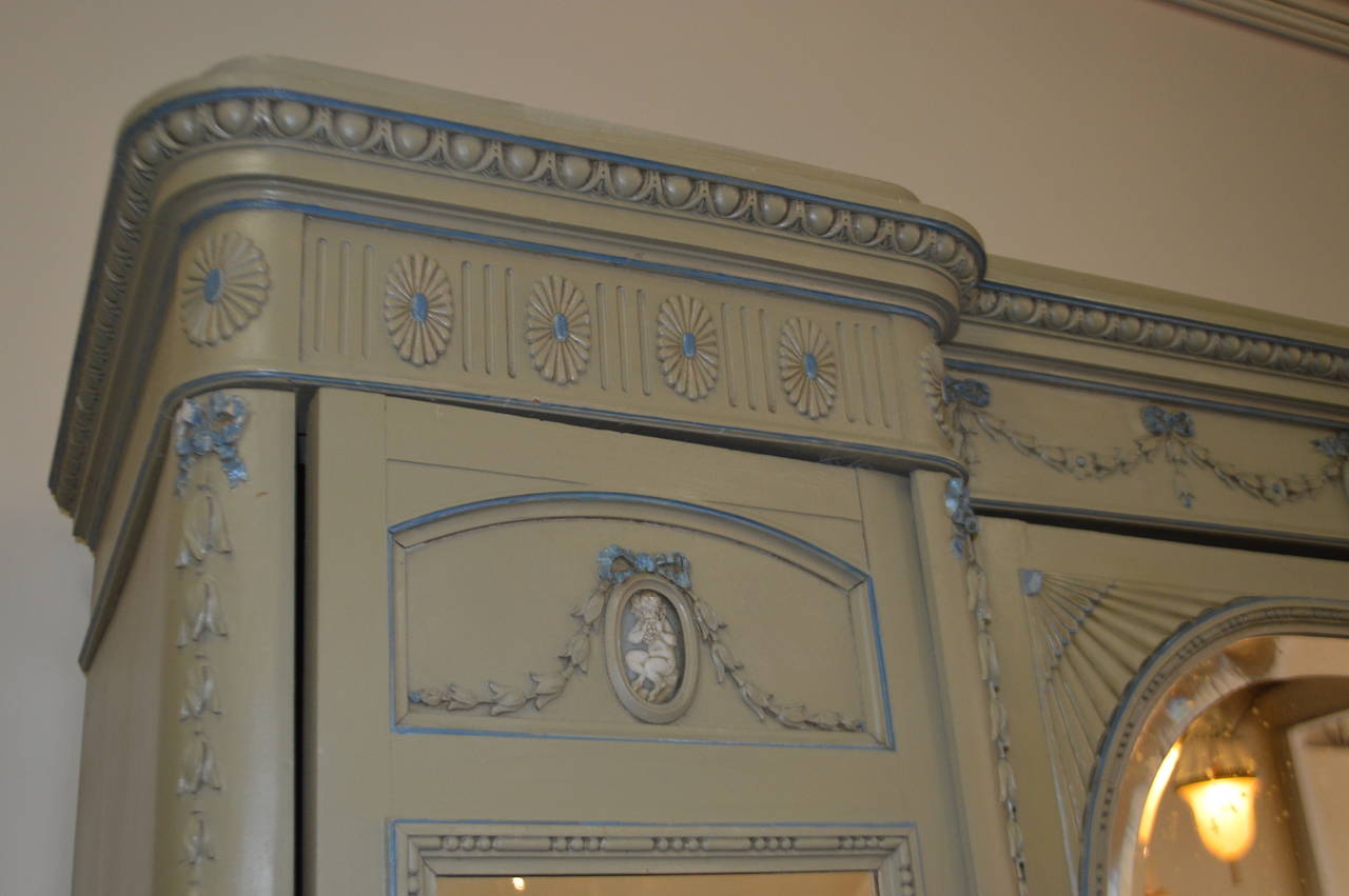 Louis XVI style painted armoire with fine hand-carved decorative details, swags and medallions. Three mirrored doors and many shelves for clothing and storage.