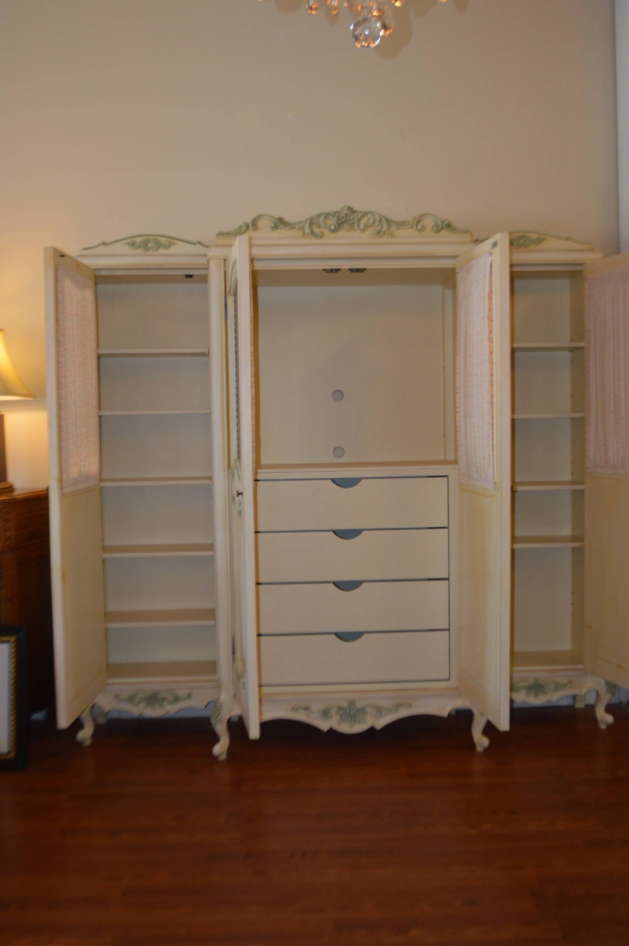 Beautiful custom built four-door armoire painted in a cream tone with amazing carved details of roses on each leg. The hand carving accents are painted in soft green. The door panels have a metal grill insert.
This armoire is most versatile, could