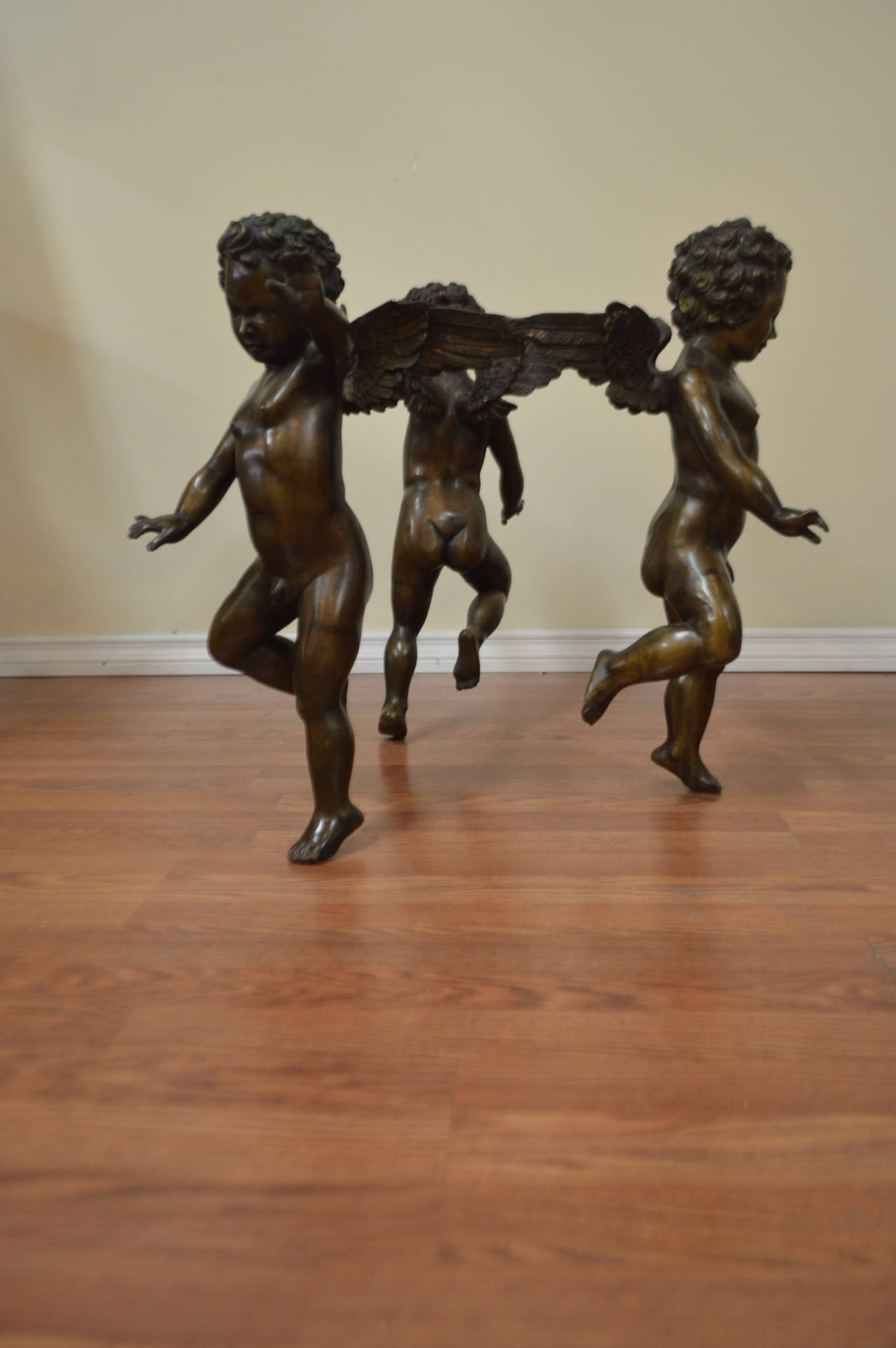 Most unusual circle formed by three bronze cherubs joined at their wings to hold a glass top cocktail table.